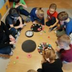 Na podłodze dzieci robią zegary, kleją kolorowe kółeczka z numerami, wskazówki. W środku leży prawdziwy zegar.